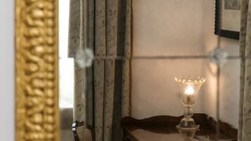 Un espejo con un marco dorado ornamentado refleja una habitación con una mesa, cortinas y un cuadro colgado en la pared.
