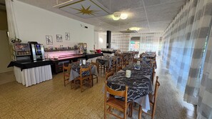 Un restaurante con mesas y sillas de tablero de mármol, una máquina de café y obras de arte en las paredes.