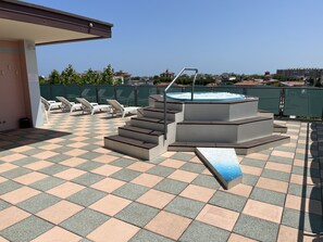 Zona de piscina en la azotea con jacuzzi, sillones de descanso y una escalera que lleva a un nivel superior.