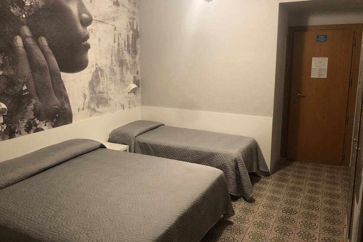 Une chambre avec deux lits, une grande peinture abstraite au mur, une porte avec une pancarte et un tapis à motifs.