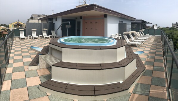 Un área de piscina en la azotea con un jacuzzi, sillas de descanso y piso a cuadros.