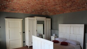 Un dormitorio con techo de ladrillo, muebles blancos y una cama con ropa de cama floral.