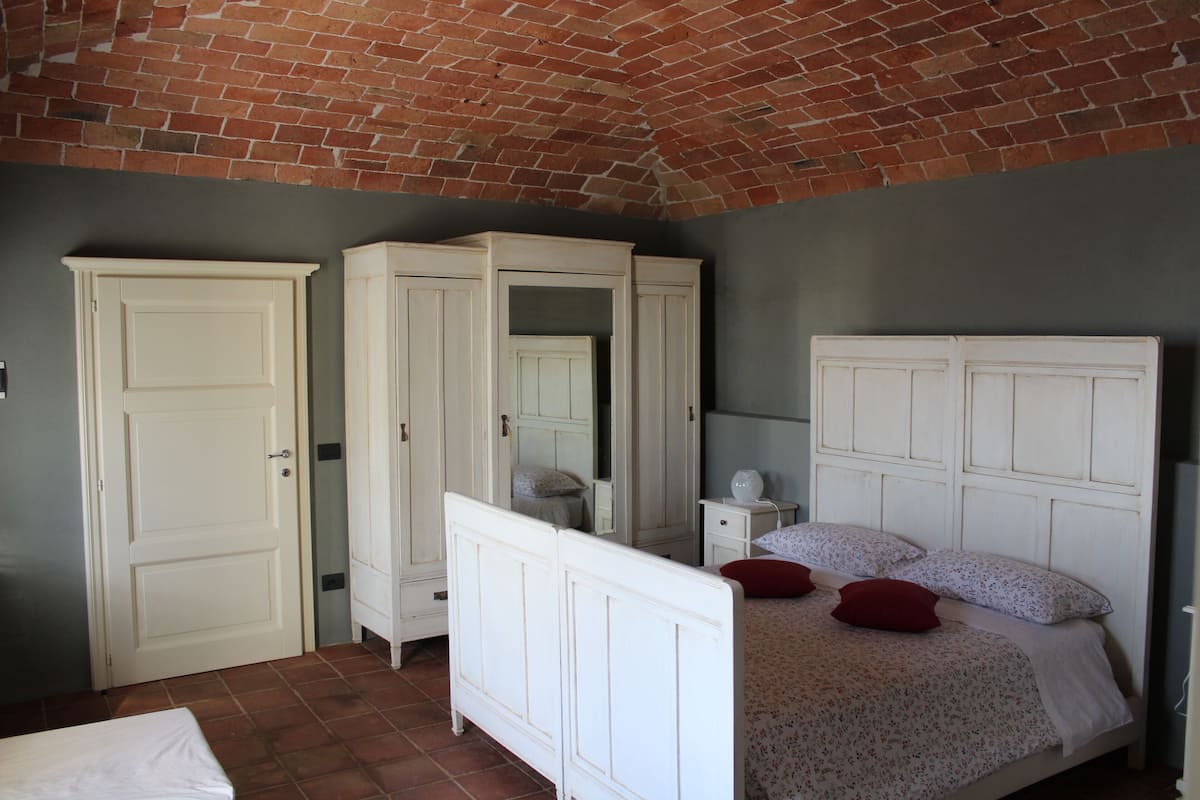 Un dormitorio con techo de ladrillo, muebles blancos y una cama con ropa de cama floral.