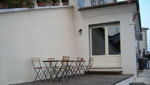 Un patio con una mesa y sillas, una puerta blanca y unos pocos escalones que llevan a la puerta.