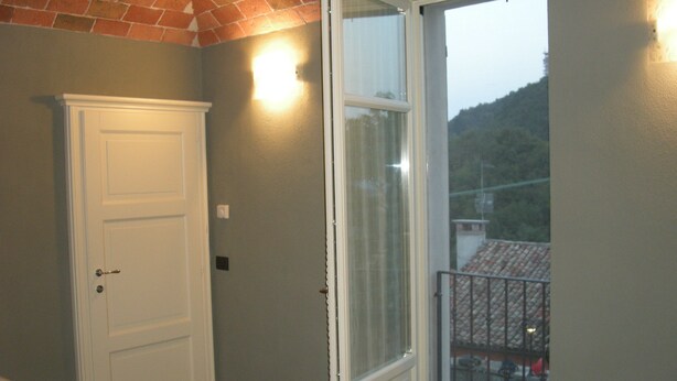 Una habitación con puerta, ventana y vistas a un balcón, además de un aplique en la pared.