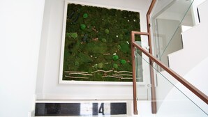 Un interior moderno con barandilla de vidrio, un cuadro de arte con motivos vegetales y una puerta blanca.