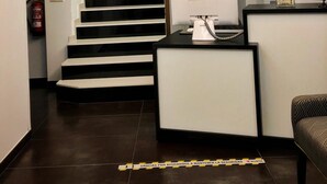 Un área de recepción moderna con una escalera, un mostrador con una computadora y un arreglo decorativo de plantas.