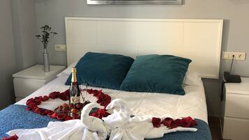 A neatly made bed with a blue blanket, white pillows, and a bouquet of red roses.