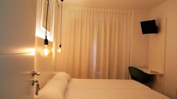 Habitación de hotel con cama, escritorio con silla, televisor montado en la pared y ventana con cortinas.