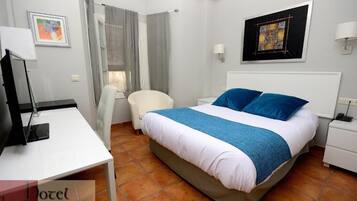 Une chambre d’hôtel avec un lit, un bureau, une chaise, une table de chevet et une fenêtre avec des rideaux.