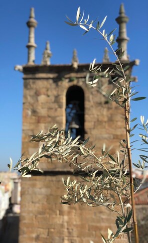 A stone tower with a central arched window and multiple pinnacles, surrounded by olive branches. - Hotel La Encomienda (Moraleja)