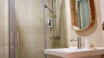 Un baño con ducha de vidrio, lavamanos con espejo y perchero para toallas.