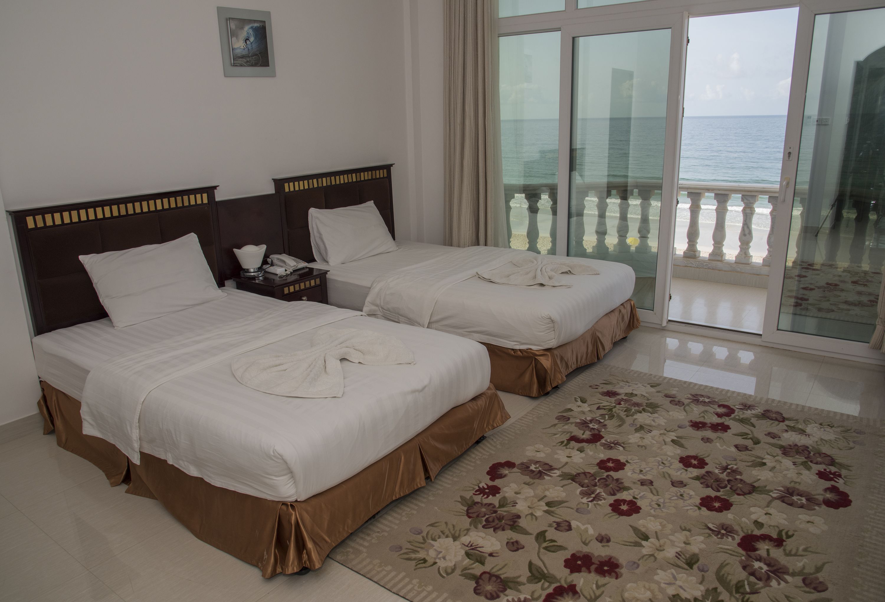 A hotel room with two beds, a floral rug, and a balcony with a view of the sea.