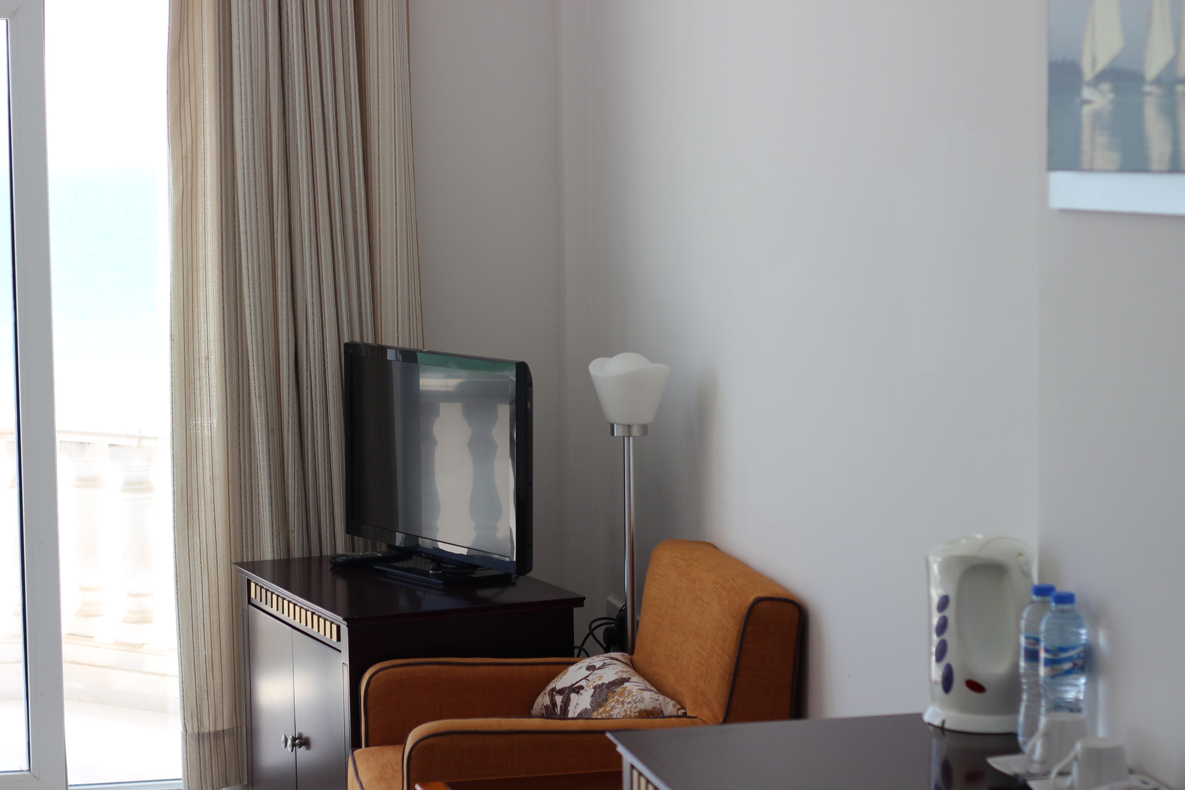 A hotel room with a television on a cabinet, an orange chair, a lamp, and a water dispenser.