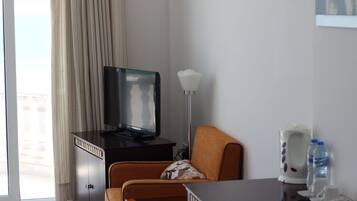 A hotel room with a television on a cabinet, an orange chair, a lamp, and a water dispenser.