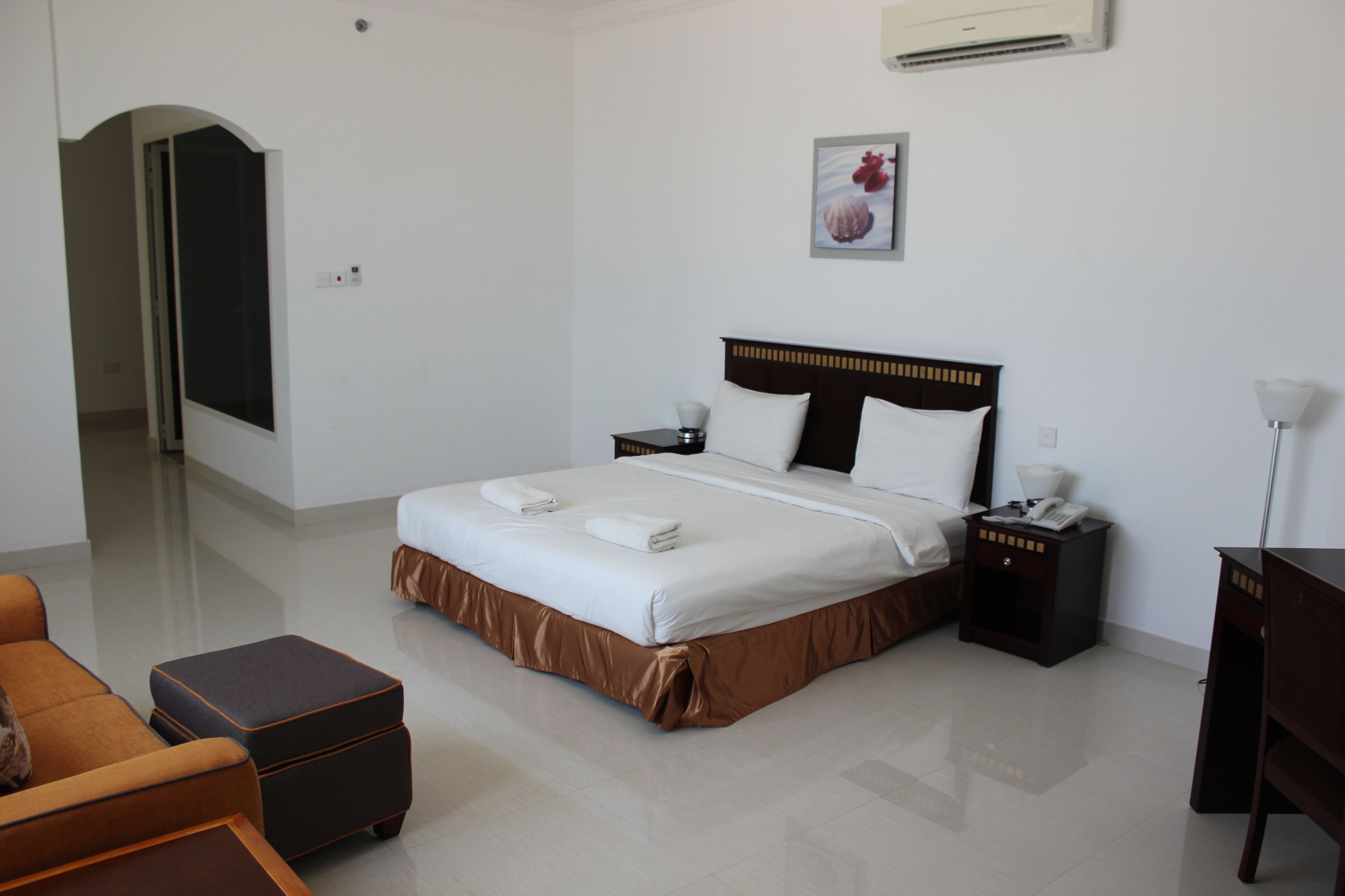 A hotel room with a large bed, a nightstand, a desk, a chair, and a door leading to another room.