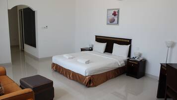 A hotel room with a large bed, a nightstand, a desk, a chair, and a door leading to another room.