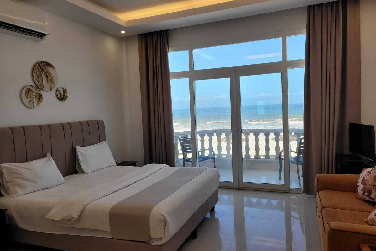 Une chambre d’hôtel avec un grand lit, une télévision et vue sur la plage.