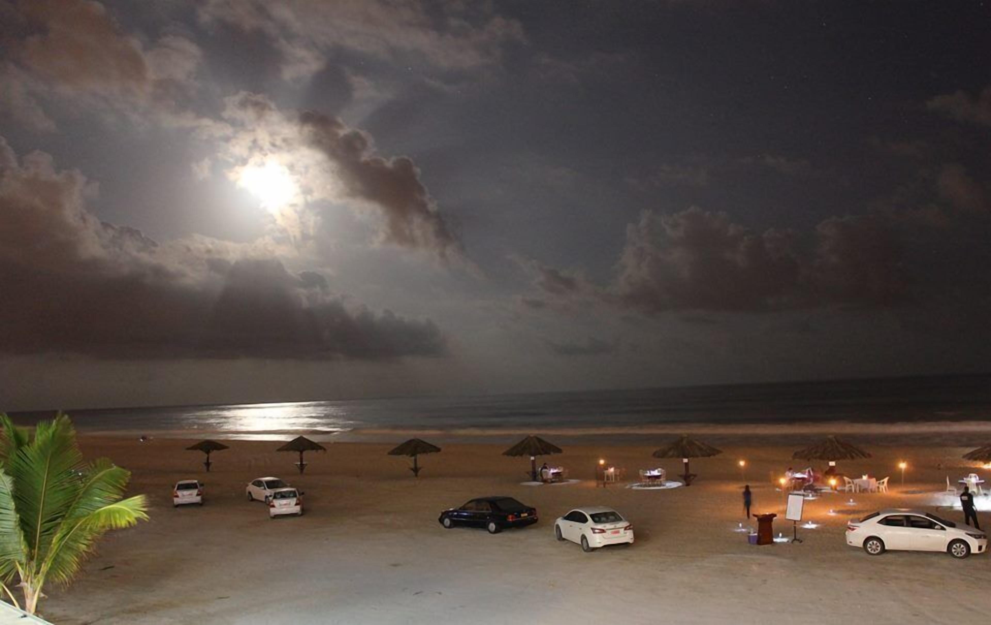 Una playa con sombrillas y coches estacionados en la arena, un cielo iluminado por la luna y un mar tranquilo.