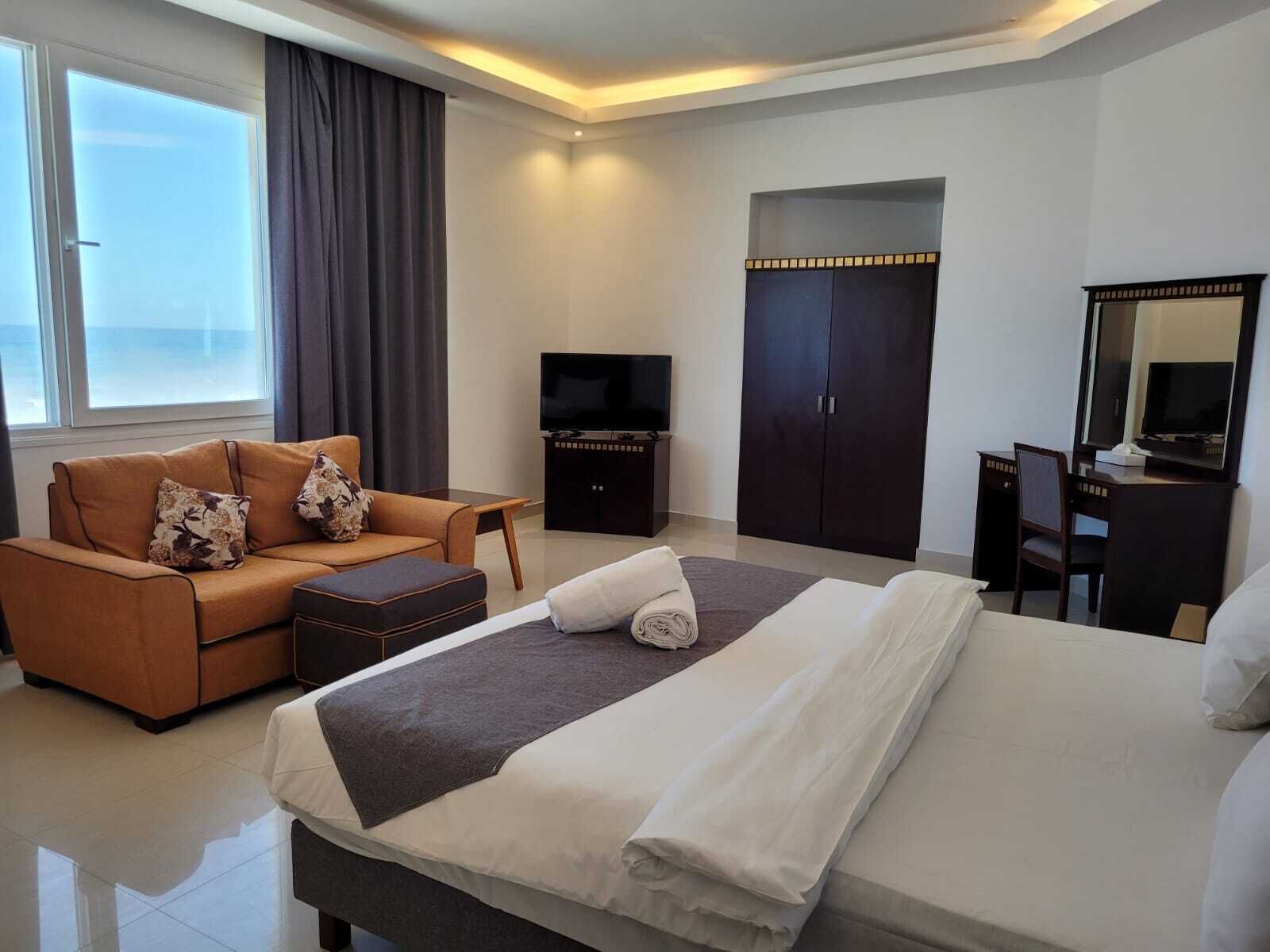 A hotel room with a bed, a sofa, a TV, a desk, and a wardrobe.