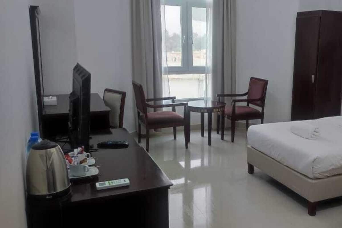 Une chambre d’hôtel comprenant un lit, un bureau avec un ordinateur, une chaise, une armoire et une fenêtre.