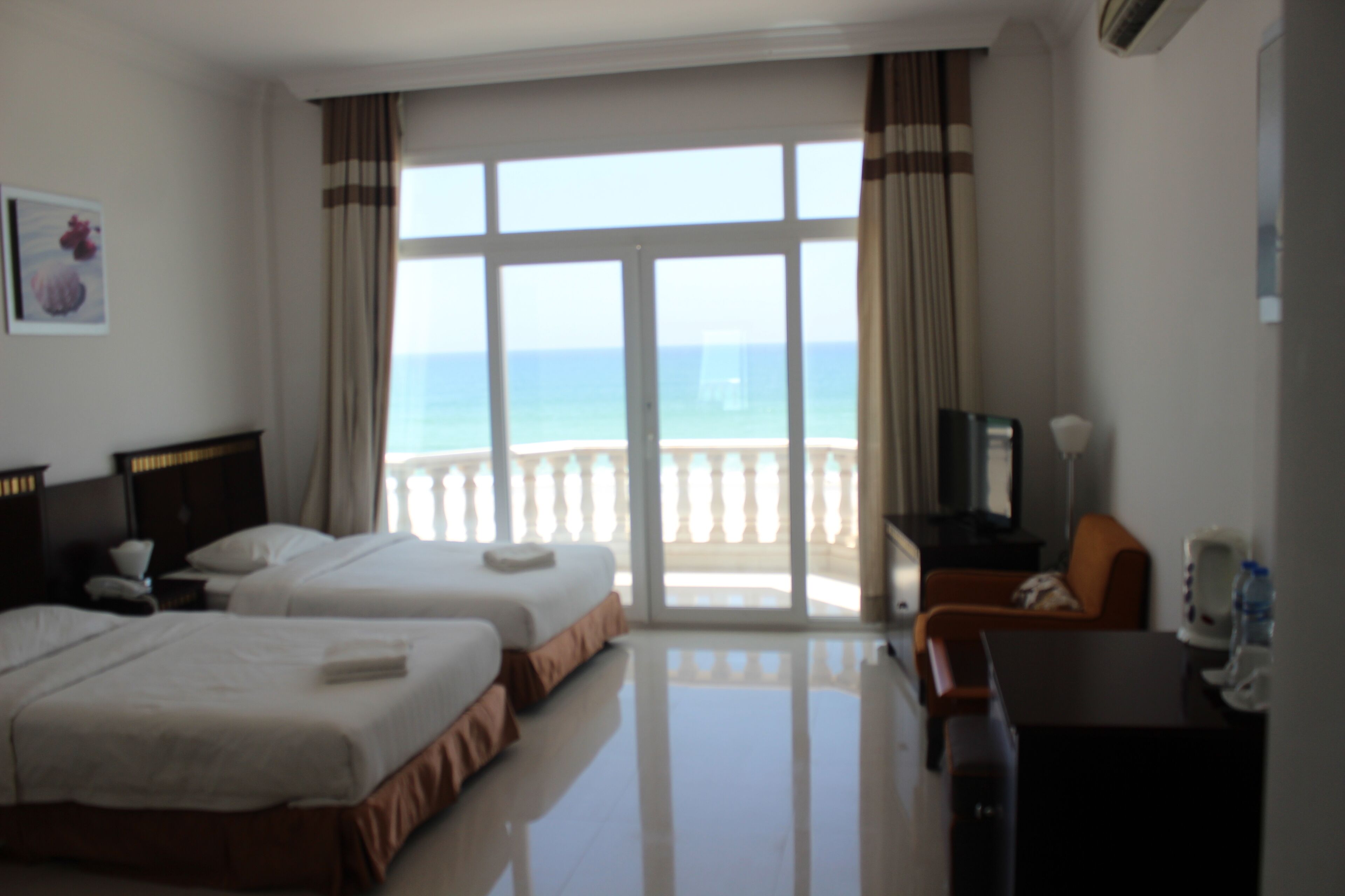 A hotel room with two beds, a desk, a chair, a TV, and a view of the ocean.