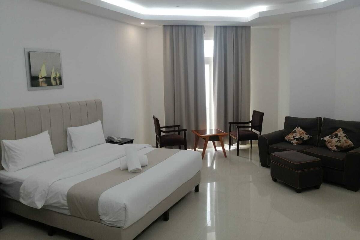 Une chambre d’hôtel moderne, dotée d’un grand lit, d’un canapé, de deux fauteuils, d’une petite table et d’un tableau au mur.