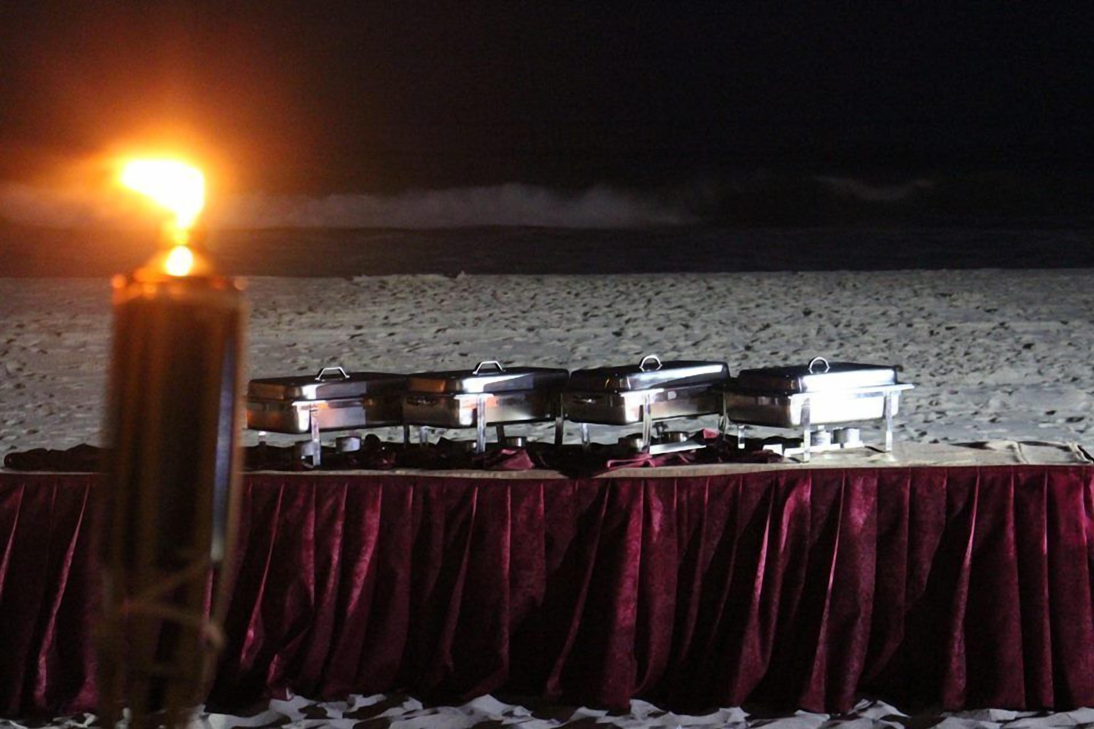 A table with a red tablecloth and several electronic devices, possibly for audio or video equipment, on a beach at night.