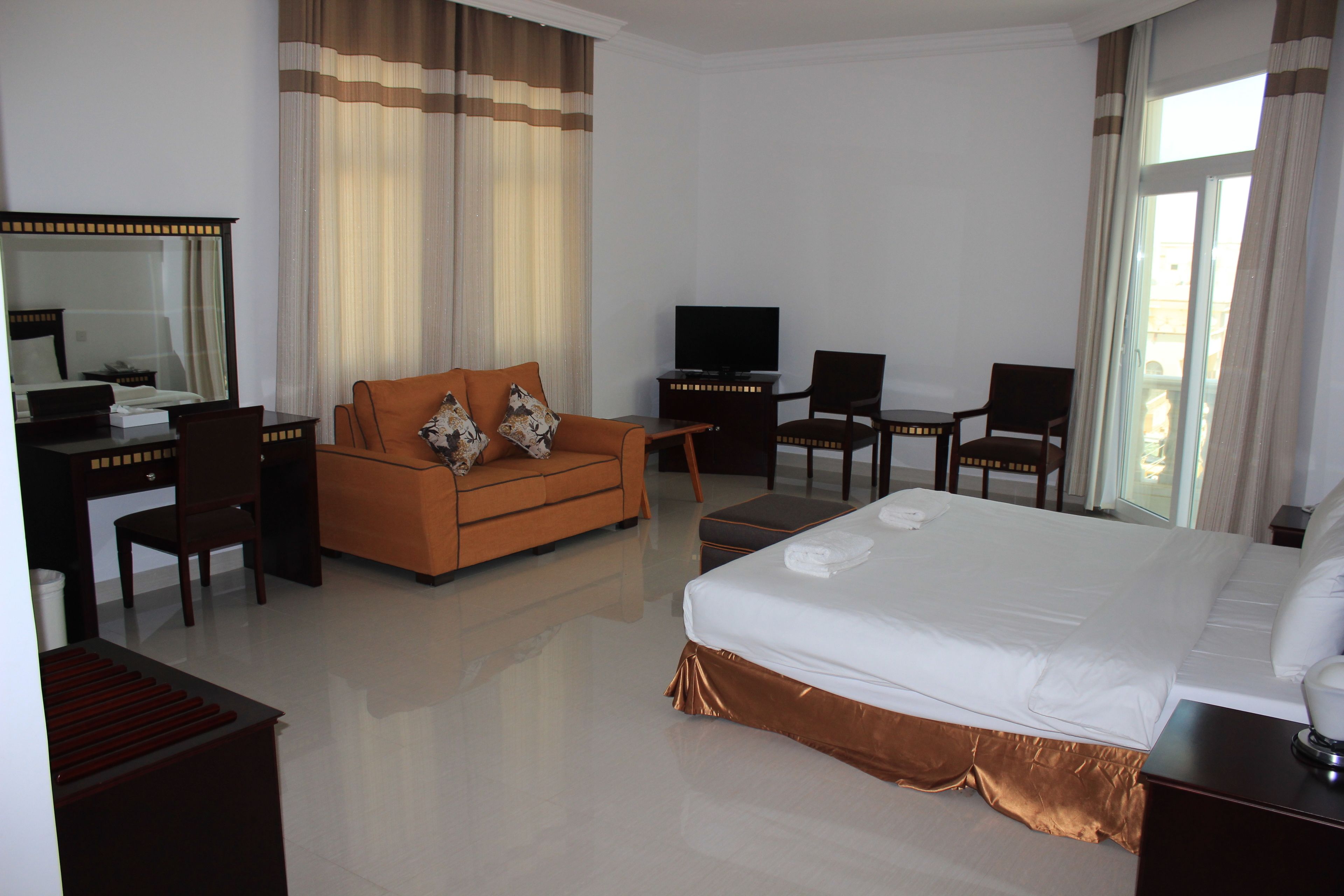 A hotel room with a large bed, a sofa, a desk with a computer, a TV, and a small table.