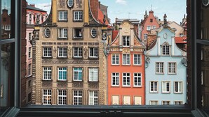 A view through a window of colorful buildings with distinct architectural styles, including a building with a clock and another with a statue on the roof. - B&B HOTEL Gdańsk Old Town (Gdansk)