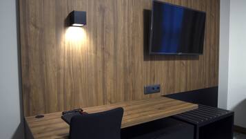 Una habitación moderna con una pared de madera, un televisor montado, un escritorio con una silla y un estante pequeño.