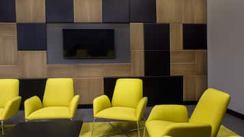 A conference room with a large flat-screen TV mounted on a wall with wooden panels. There are four yellow chairs around a black table.