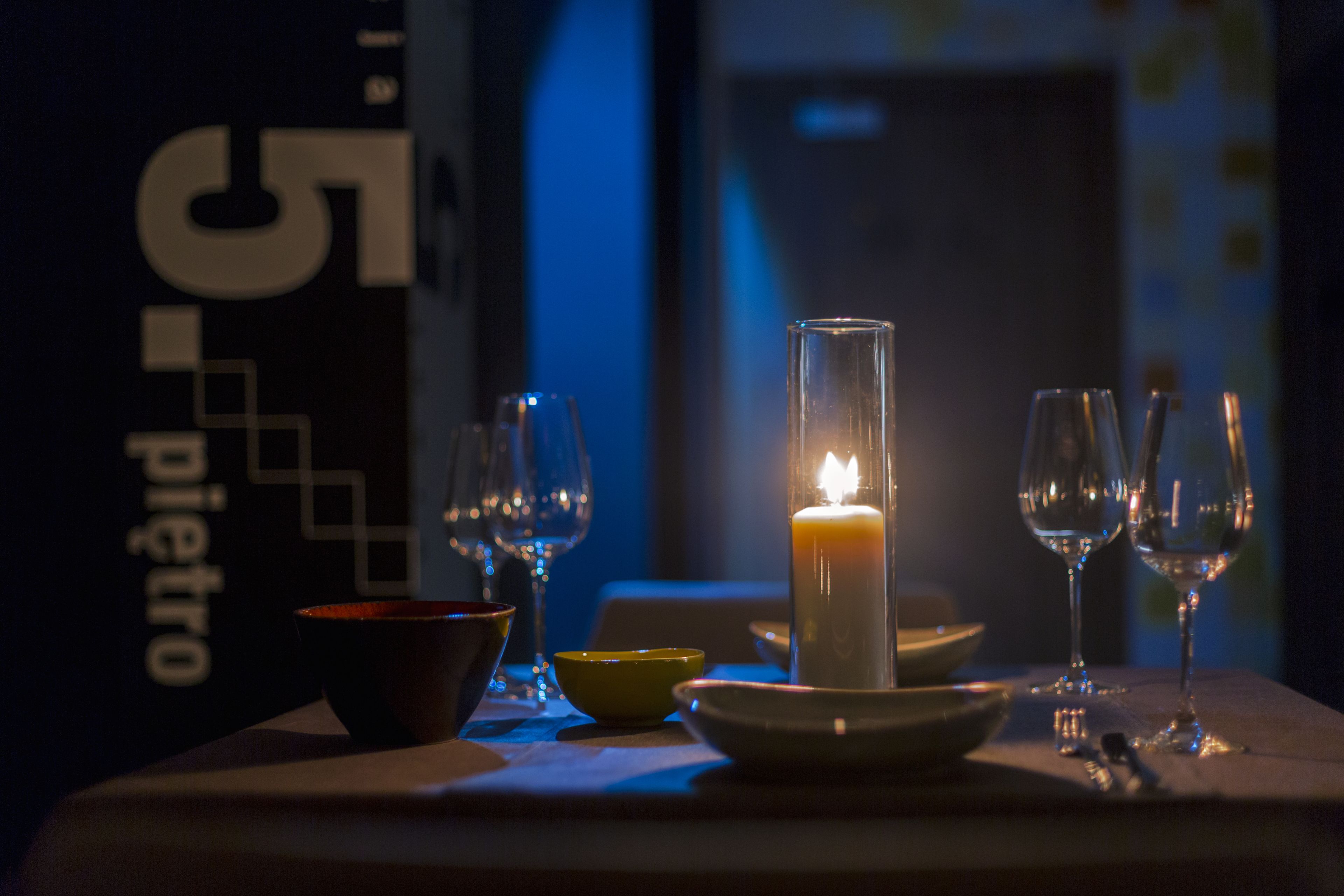 A candlelit table with glasses and bowls, a sign with '55' and 'pietro' visible, and a dimly lit background.