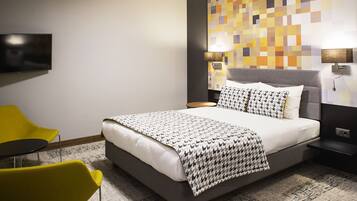 A modern hotel room with a large bed, a flat-screen TV, two bedside tables, and a yellow chair.