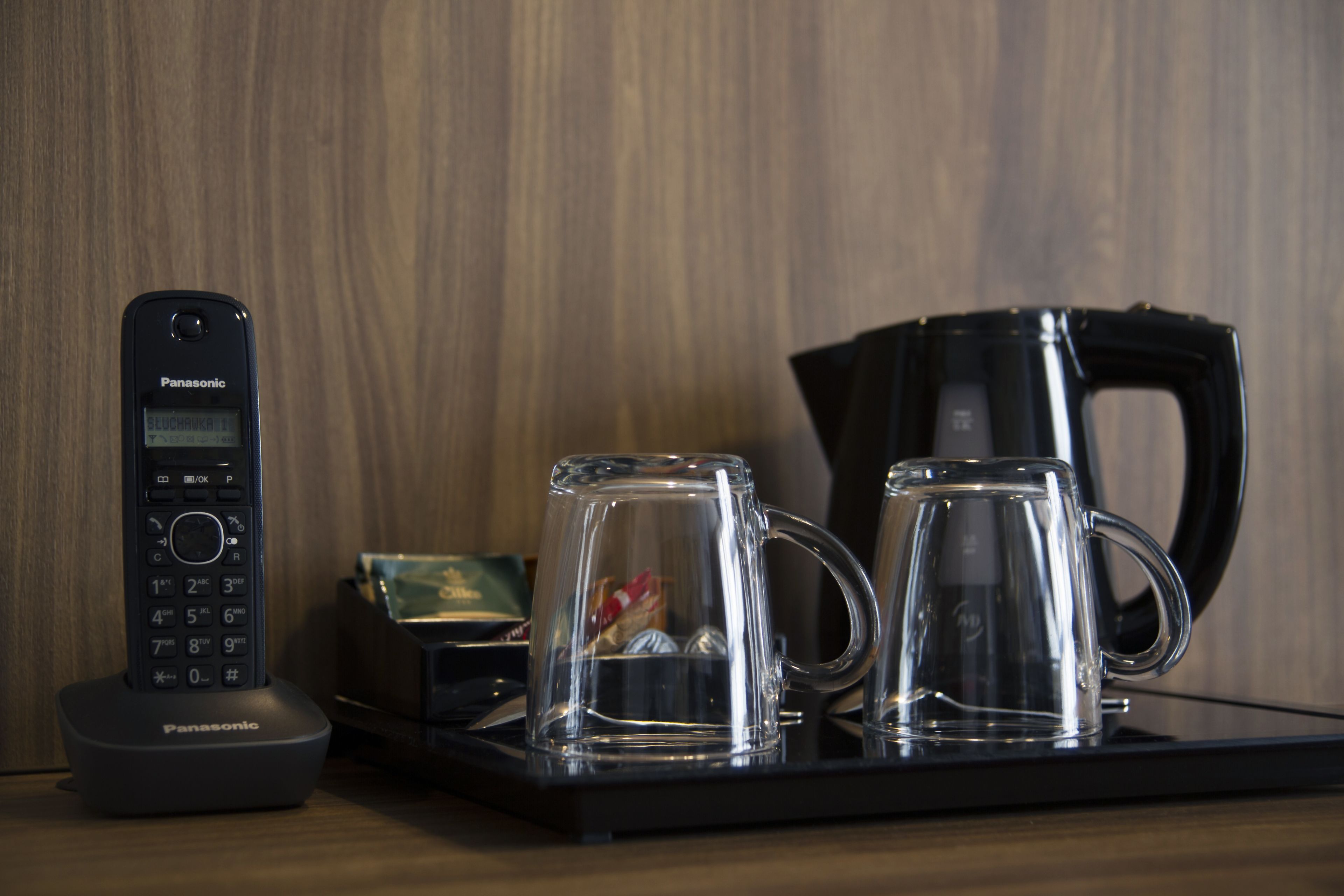 A Panasonic cordless phone on a charging dock, two clear glass mugs, and a black coffee maker on a tray.