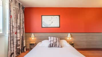 A hotel room with a bed, two bedside tables with lamps, a framed artwork on the wall, and a window with curtains.