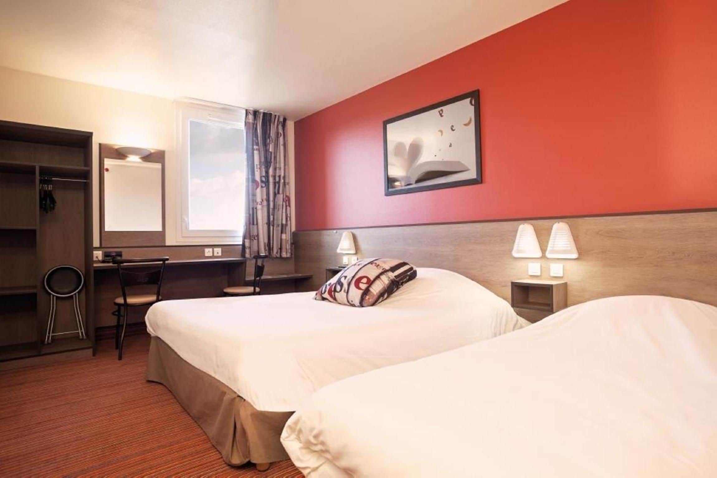 A hotel room with two beds, a desk, a chair, a mirror, and a window with curtains.