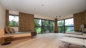 Una habitación moderna con ventanas amplias, suelo de madera, un banco y una mesa.