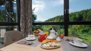 Una mesa de desayuno con pasteles, café y jugo, con vistas a árboles y montañas.