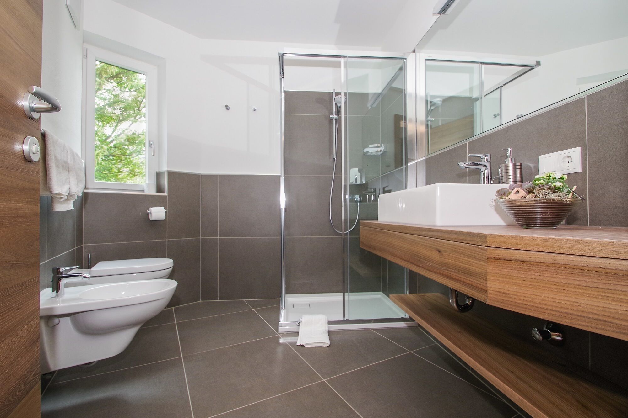 A modern bathroom with a glass shower enclosure, a white toilet, and a wooden vanity with a sink.