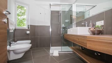 A modern bathroom with a glass shower enclosure, a white toilet, and a wooden vanity with a sink.