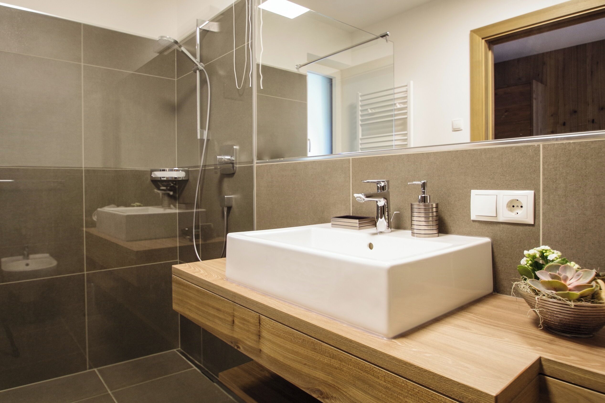 A modern bathroom with a large rectangular sink, a glass shower enclosure, and a wooden vanity.