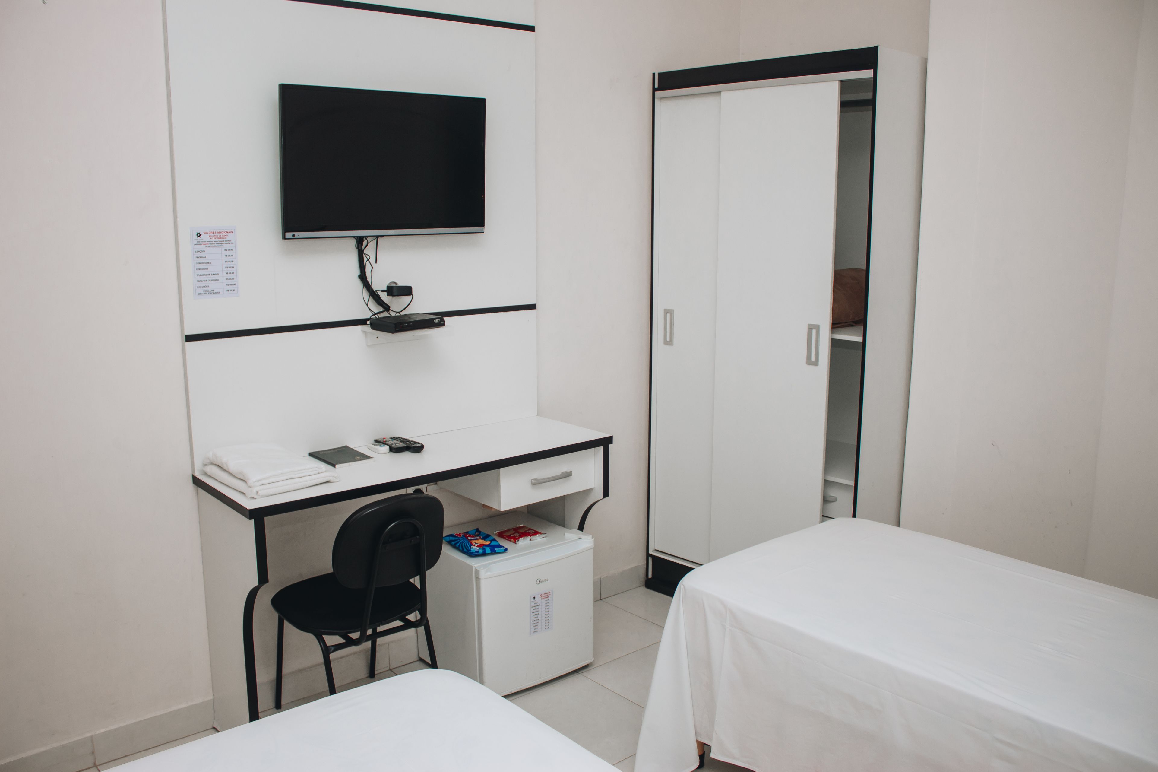 Habitación de hotel con escritorio, una silla, cama, armario y televisor.
