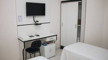 A hotel room with a desk, a chair, a bed, a wardrobe, and a television.