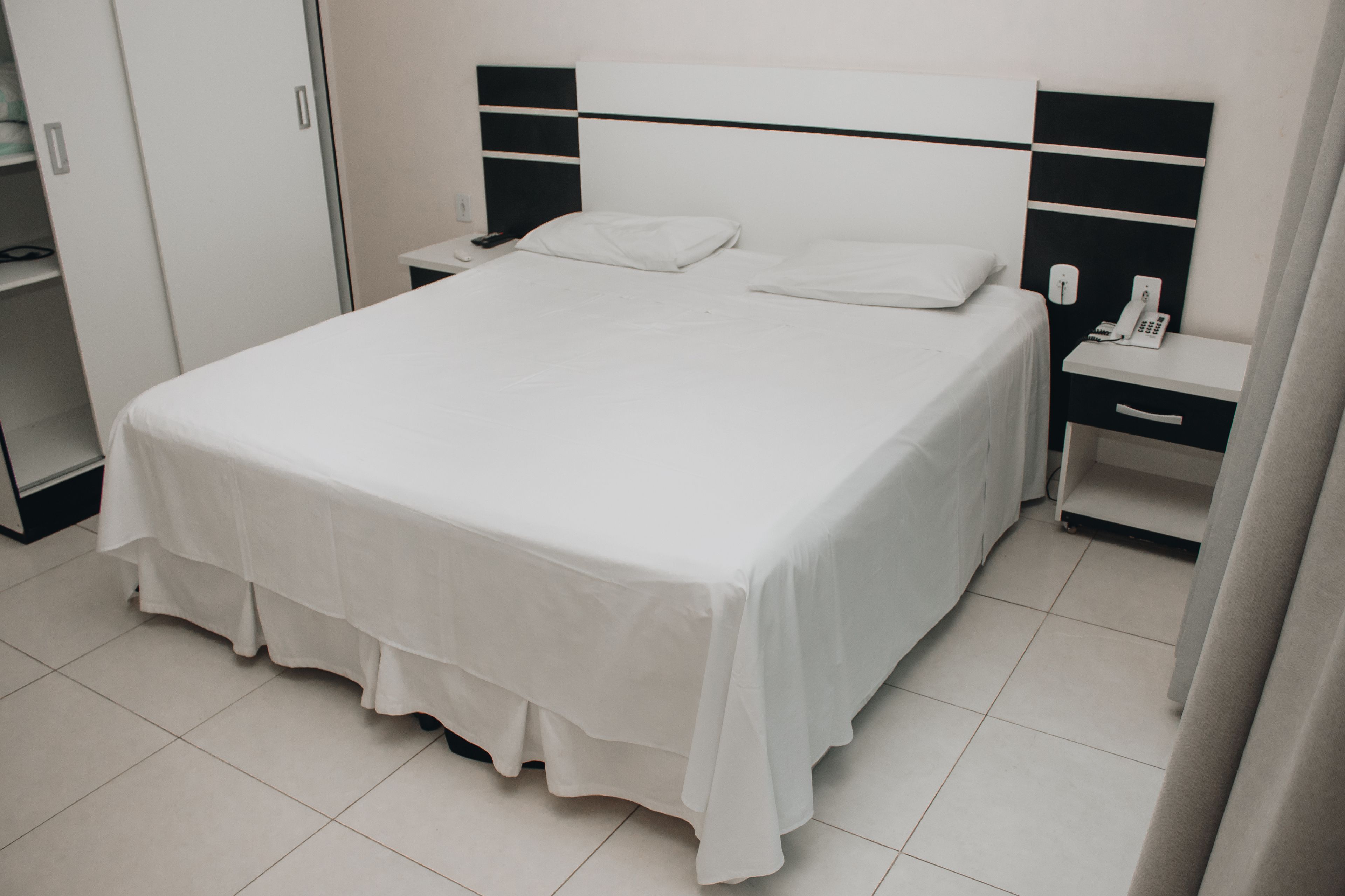 Una cama bien hecha con ropa blanca, una mesita de noche con un teléfono y una mesita con una lámpara.
