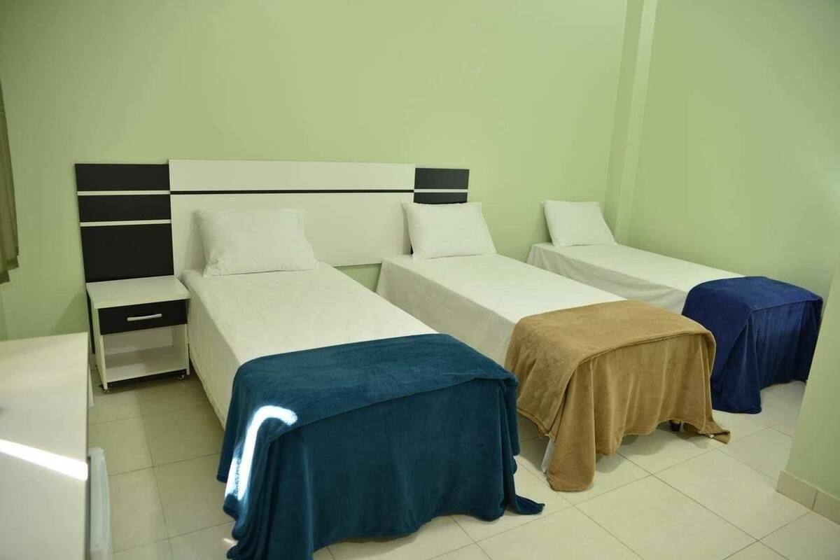 A hotel room with two single beds, a small bedside table, and a desk with a chair.
