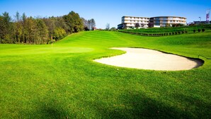 A golf course with a sand bunker, a flagstick, and a building in the background. - Hotel der Freiraum (Guessing)