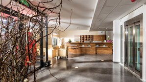 A modern reception area with a wooden reception desk, a seating area, and a glass elevator. - Hotel der Freiraum (Guessing)