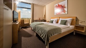 A hotel room with a large bed, a television, a desk, and a window with a view. - Hotel der Freiraum (Guessing)