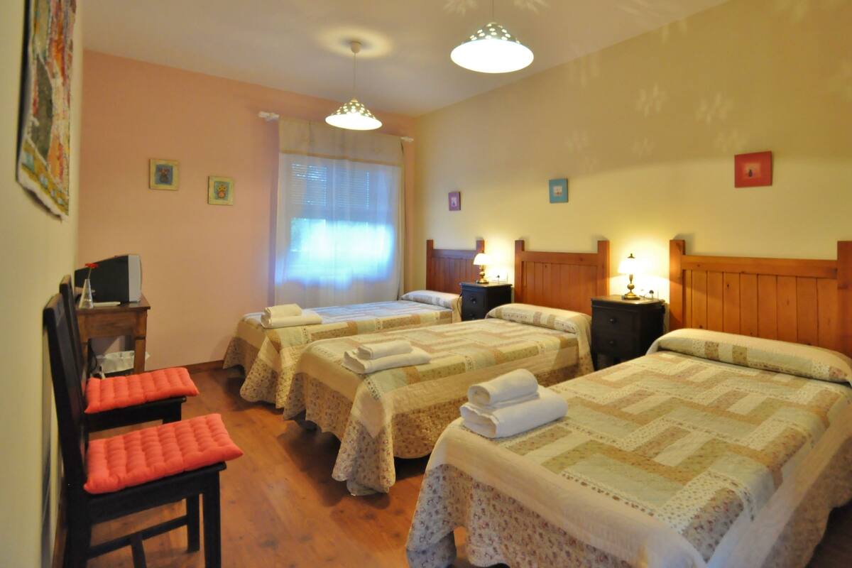 A hotel room with two beds, a wooden headboard, a desk with a chair, and a window with curtains.